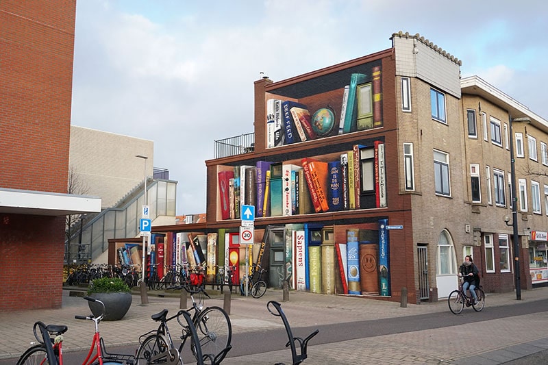 Read more about the article Street Artist transforms gray city walls into beautiful giant bookcases to promote diversity
